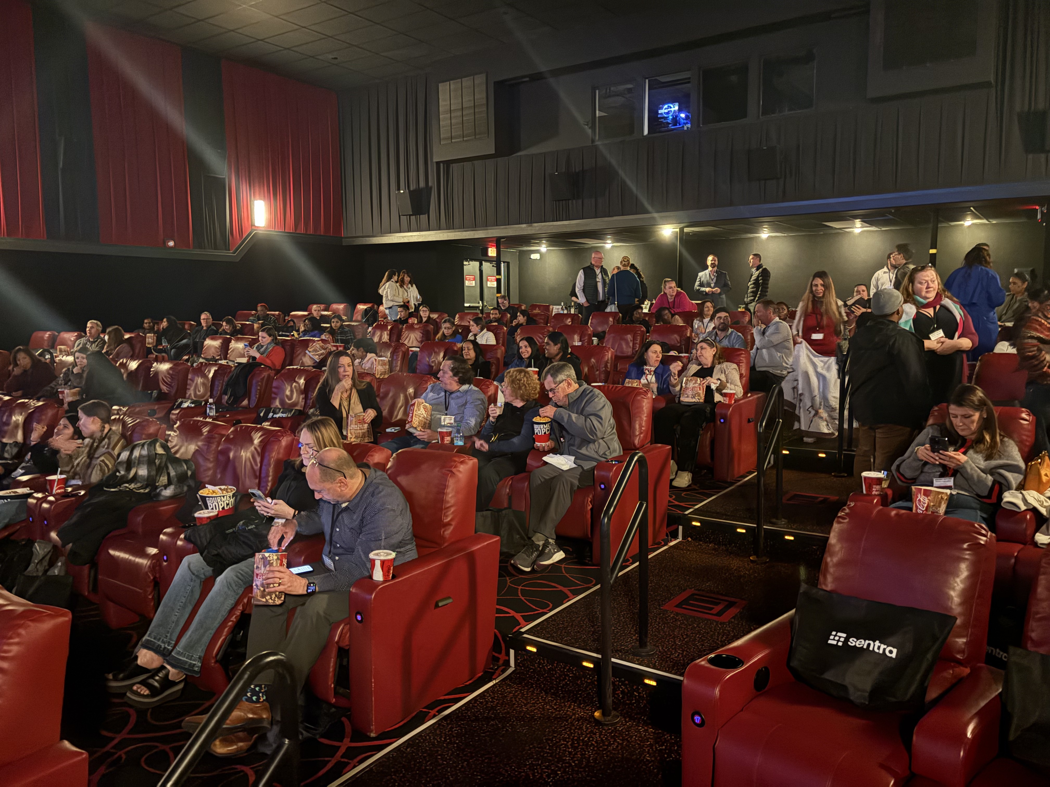 A theater full of red recliner seats and audience